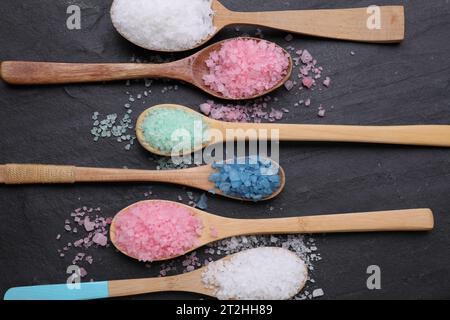 Löffel mit verschiedenen Meersalzen auf schwarzem Tisch, flach gelegt Stockfoto