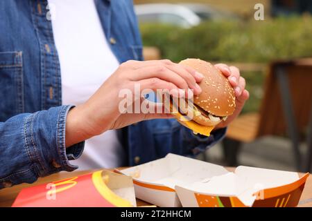 Lemberg, Ukraine - 9. Oktober 2023: Frau mit McDonald's Burger am Tisch draußen, Nahaufnahme Stockfoto