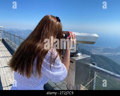 Frau, die durch Teleskop auf die bewölkten Berge blickt. Stockfoto