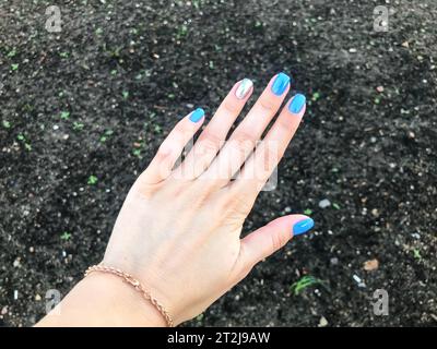 Hellblaue und glänzende silberne Nägel auf der Hand des Mädchens mit einem goldenen Armband. Schöne lange Finger des Mädchens. Schöne Maniküre unter schwarzem Boden im Stockfoto