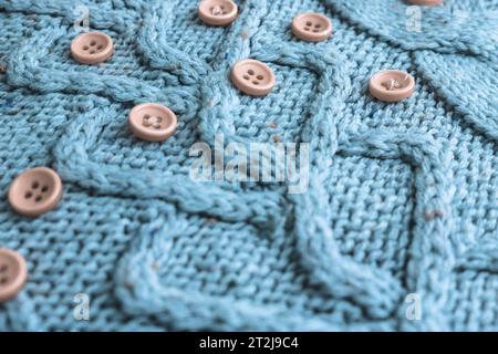 Schöne Textur eines weichen, warmen Naturpullovers mit einem Strickmuster aus Garn und roten kleinen runden Knöpfen zum Nähen. Der Hintergrund. Stockfoto