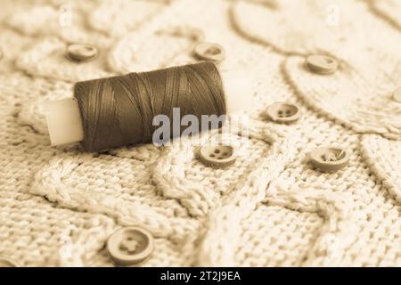 Eine schöne Sepia-Textur ist ein weicher, warmer natürlicher Pullover, Stoffe mit einem Strickmuster aus Garn und roten kleinen runden Knöpfen zum Nähen und einem Knäuel von Stockfoto