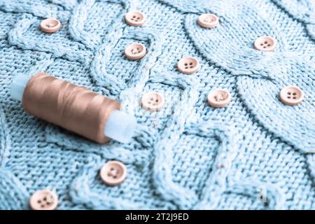 Schöne Textur eines weichen, warmen Naturpullovers, Stoffe mit einem Strickmuster aus Garn und roten kleinen runden Knöpfen zum Nähen und einem Knäuel aus rotem Thr Stockfoto