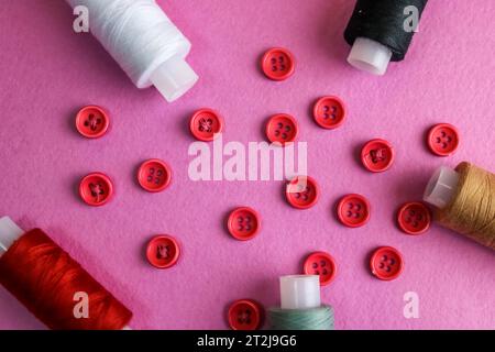 Schöner Rahmen mit vielen runden roten Knöpfen zum Nähen, Handarbeiten und Fadenspulen. Kopierbereich. Flache Lagen. Lila rosa Hintergrund. Stockfoto