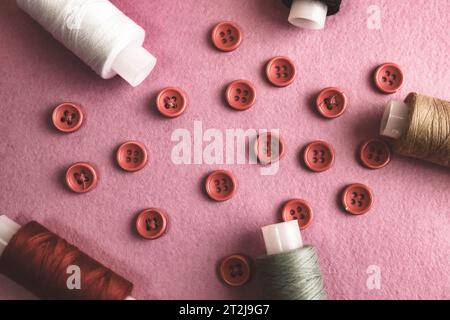 Schöner Rahmen mit vielen runden roten Knöpfen zum Nähen, Handarbeiten und Fadenspulen. Kopierbereich. Flache Lagen. Lila rosa Hintergrund. Stockfoto