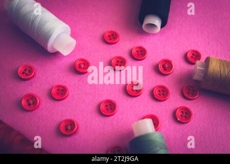 Schöner Rahmen mit vielen runden roten Knöpfen zum Nähen, Handarbeiten und Fadenspulen. Kopierbereich. Flache Lagen. Lila rosa Hintergrund. Stockfoto