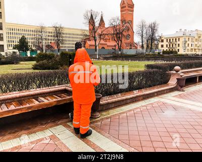 Männliche Arbeitsreiniger in orangefarbenen Overalls in Bademantel Arbeit reinigt die Straßen der Stadt. Stockfoto