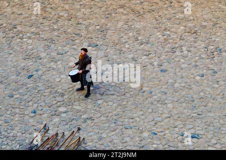 Ein schottischer Krieger, Soldat, Musiker mit rotem Bart in traditioneller Tracht und Rock schlägt die Trommel auf dem Platz einer mittelalterlichen alten Burg. Nesv Stockfoto