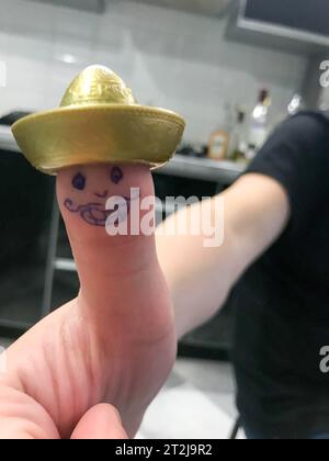 Daumen, Finger Mexikaner im goldenen Hut Sombrero mit gemaltem fröhlichem Gesicht mit Schnurrbart und Augen. Stockfoto