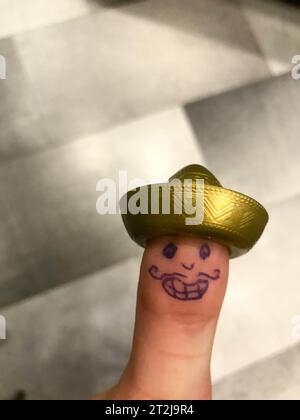 Daumen, Finger Mexikaner im goldenen Hut Sombrero mit gemaltem fröhlichem Gesicht mit Schnurrbart und Augen. Stockfoto