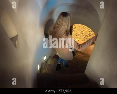 Ein Mädchen, eine Frau, steigt die steile Steinspiraltreppe hinunter, die schmalen Stufen hinunter. Stockfoto