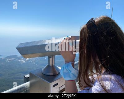 Das Mädchen schaut von einer großen Festungsmauer in Antalya in der Türkei auf die Berge und den Himmel. Es benutzt ein Monokular, ein Teleskop, ein Fernglas Stockfoto