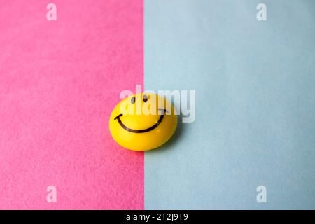 Runde Plastikgelb fröhlich lächelndes Spielzeug rundes Gesicht Emoji auf einem rosa blauen violetten Hintergrund. Stockfoto