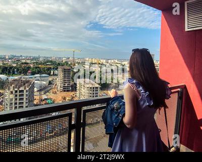 Bau eines neuen Wohnkomplexes in der Innenstadt. Blick auf die Baustelle von oben. Ein Mädchen mit langen, dunklen Haaren auf dem Balkon wat Stockfoto