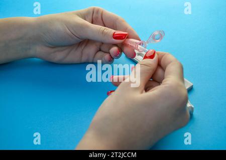 Medizinische Diagnostik. Mädchen mit roter Maniküre hält eine Lanzette für ein Fingerpiercing. Kapillarblut, Diagnostik ihrer Gesundheit zur Identifizierung einer Infektion Stockfoto