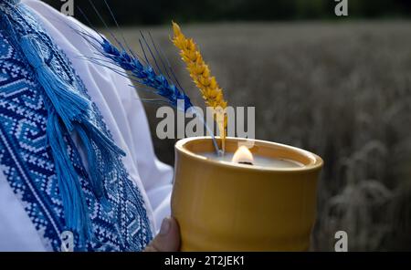 Brennende Kerze, ein aufgesticktes ukrainisches Hemd und zwei Maisohren, bemalt in gelb-blauen Farben der ukrainischen Flagge Stockfoto