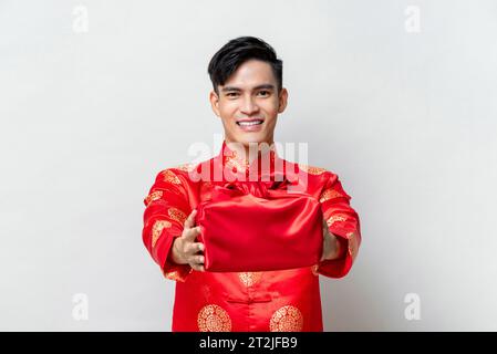 Hübscher lächelnder asiatischer Mann, der chinesisches Neujahrsgeschenk in isoliertem hellgrauen Hintergrund gibt Stockfoto