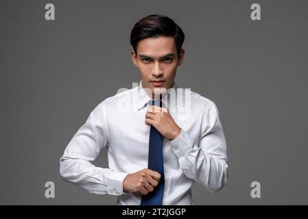 Selbstbewusster junger asiatischer männlicher Unternehmer in weißem Hemd, der auf grauem isoliertem Atelierhintergrund steht Stockfoto