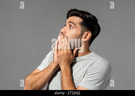 Überraschter kaukasischer Bart, der den Mund auf grauem, isoliertem Hintergrund im Studio bedeckt Stockfoto