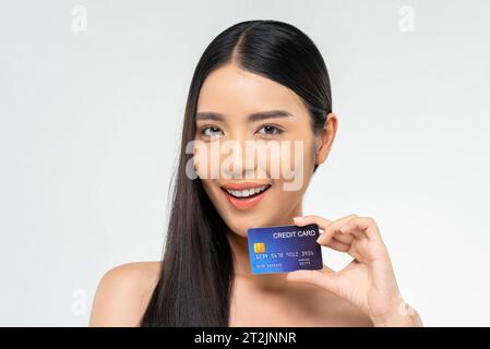 Schönheitsaufnahme der fröhlichen asiatischen Frau mit langen dunklen Haaren, die Kreditkarte auf weißem isoliertem Hintergrund im Studio zeigt Stockfoto