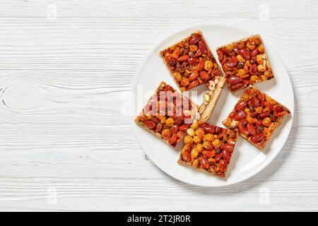 Hausgemachte Toffee gemischte Nüsse Shortbread Bars auf weißem Teller auf weißem Holztisch, horizontaler Blick von oben, flache Lagen, freier Platz Stockfoto