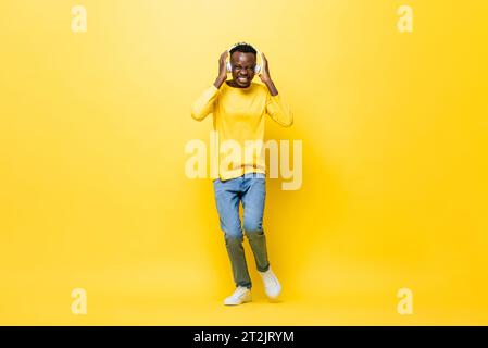 Porträt eines glücklichen lächelnden jungen afrikanischen Mannes, der Musik von Kopfhörern hört und im gelben Studio tanzt Stockfoto
