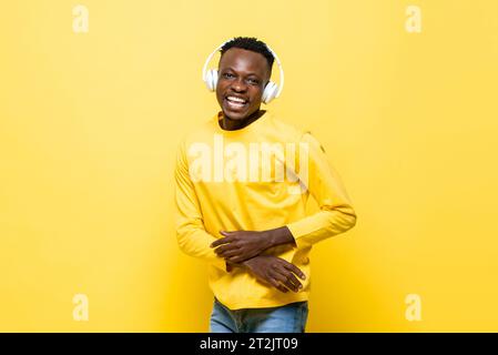 Junger fröhlicher afrikanischer Mann, der Kopfhörer trägt, Musik hört und tanzt in isoliertem gelben Farb-Studio-Hintergrund Stockfoto