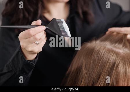 Ein professioneller Friseur trägt Haarfarbe mit einer Bürste auf einen Kunden in einem Schönheitssalon auf Stockfoto