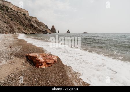 Großer roter Jasperstein am Strand, mit Meer im Hintergrund. Big Red Jasper Stone Nahaufnahme Stockfoto