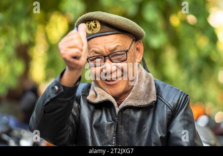 Ein älterer vietnamesischer Mann mit olivgrüner Baskenmütze und Lederjacke gibt in Hanoi, Vietnam, die Daumen hoch. Stockfoto