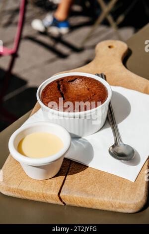 Genießen Sie einen köstlichen Schokoladen-Brownie mit Vanillesauce, serviert auf einem Holzhalter mit silbernem Löffel, in einem gemütlichen Hipster-Café im Freien Stockfoto