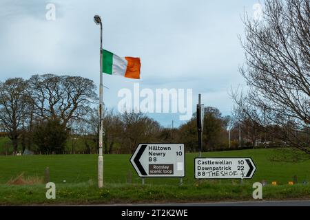 Die Flagge der Republik Irland fliegt über Straßenschildern, mit skurrilen Graffitis, die für einen lokalen Pub außerhalb von Hilltown, Co. Werben. Nach Unten Stockfoto