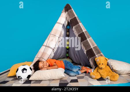 Foto des kleinen süßen Jungen, der in diy Tipi schläft, isoliert über blauem Hintergrund Stockfoto