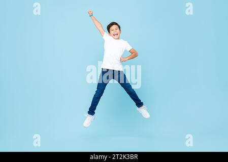 Fröhlicher asiatischer gemischter Rassenjunge, der in isoliertem hellblauem Farb-Studiohintergrund springt und die Hand hebt Stockfoto