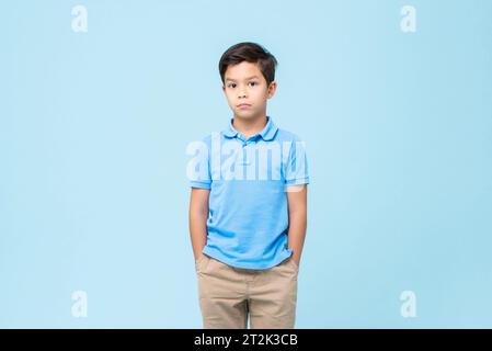 Gemischter Race Boy in legeren Kleidern, stehend mit Händen in Taschen auf hellblauem Studio isoliert schwarzem Boden Stockfoto