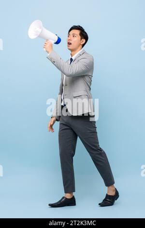 Junger gutaussehender asiatischer Mann im formellen Business-Anzug, der Megaphon in isoliertem hellblauem Farb-Studio-Hintergrund hält Stockfoto