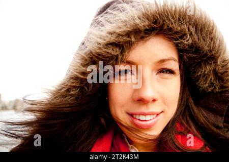 Eine Frau mit einer warmen Pelzjacke und einem roten Schal, der lächelnd ist. Stockfoto