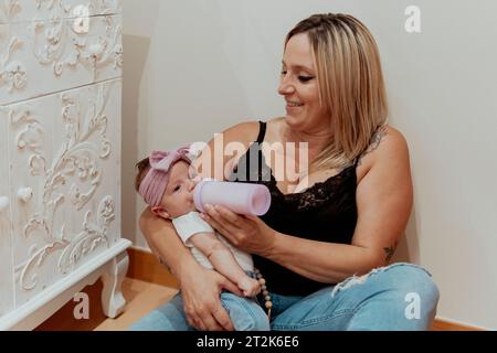 Mutter gibt dem Baby zu essen, während sie auf dem Boden sitzt Stockfoto