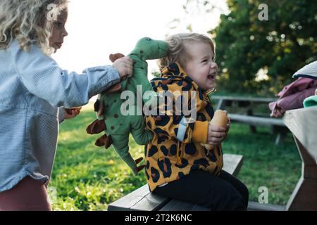 Eine ältere Schwester, die vorgibt, ein Spielzeug-Dinosaurier zu fressen, isst ihre kleine Schwester Stockfoto