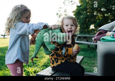 Eine ältere Schwester, die vorgibt, ihre Schwester mit einem Dinosaurier zu essen Stockfoto