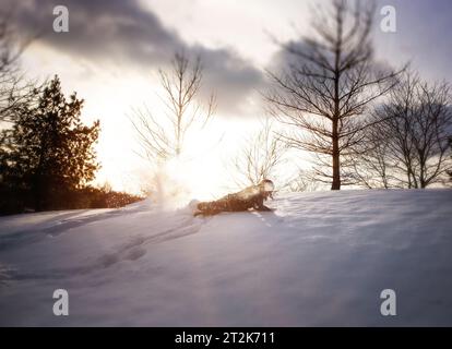 Kleines Kind, das im Winter den schneebedeckten Hügel hinunterfährt Stockfoto