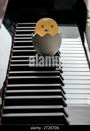 Baby-Chick-Zeichentrickfilm sitzt auf einem zerbrochenen Eierständer auf der Klaviertastatur. Gelbes süßes Huhn schlüpft aus Ei, Platz für Text, selektiver Fokus. Stockfoto