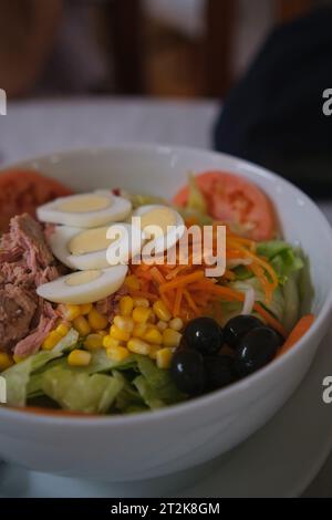 Köstlicher und frischer gemischter Salat mit Thunfisch, Tomaten, hartgekochten Eiern, Salat, Zuckermais, geriebene Karotten und schwarze Oliven. Stockfoto