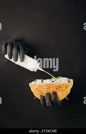 Kocht mit der Hand Soße in Döner-Döner durch gerissene Löcher auf schwarzem Papierhintergrund. Street Food Stockfoto