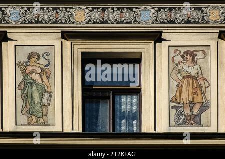 Art Nouveau-Kunstwerk, das eine Frau mit einem Caduceus und eine andere mit Hammer oder Hammer zeigt. Dekoratives Detail an der Fassade des großen Gebäudes der Neorenaissance (Ende des 19. Jahrhunderts/Anfang des 20. Jahrhunderts) auf dem Alšovo-Platz in Písek, Südböhmen, Tschechien. Stockfoto