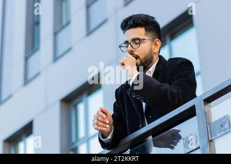 Müde erschöpfter indischer Geschäftsmann gähnt, schläfrig unaufmerksam fühlend schläfrig gelangweilt klaffend leidet unter Schlafmangel, Einschlafen draußen. Arabian Hindu Freelancer Typ in der Innenstadt Stockfoto