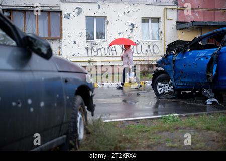 Irpin, Ukraine. Oktober 2023. Eine Frau läuft an zwei reparierten Wolkenkratzern vorbei. Im Vordergrund stehen Autos, die während des Angriffs der russischen Armee im Frühjahr 2022 zerstört wurden. Quelle: Sebastian Gollnow/dpa/Alamy Live News Stockfoto