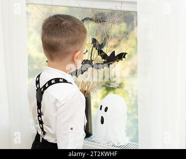 Halloween-Konzept. Keine Fläche. Die Hände des Babys in der Nähe des Fensters, vor dem Hintergrund einer Vase mit trockenen Zweigen und schwarzen Papierfledermäusen. Nahaufnahme Stockfoto