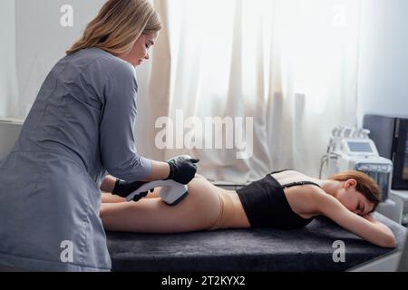 Die lächelnde Masseurin macht ihrer Klientin eine Anti-Cellulite-Gesäßmassage. Die junge Frau liegt auf dem Massagetisch und erhält eine Lymphdrainage Stockfoto