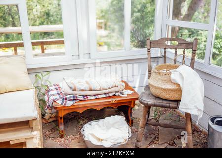 Vintage-Glaspavillon im Garten. Gemütliches Retro-Interieur mit Holzbänken und Kissen. Töpfe mit Blumen und Gartengeräten. Grüne Bäume im Backgr Stockfoto